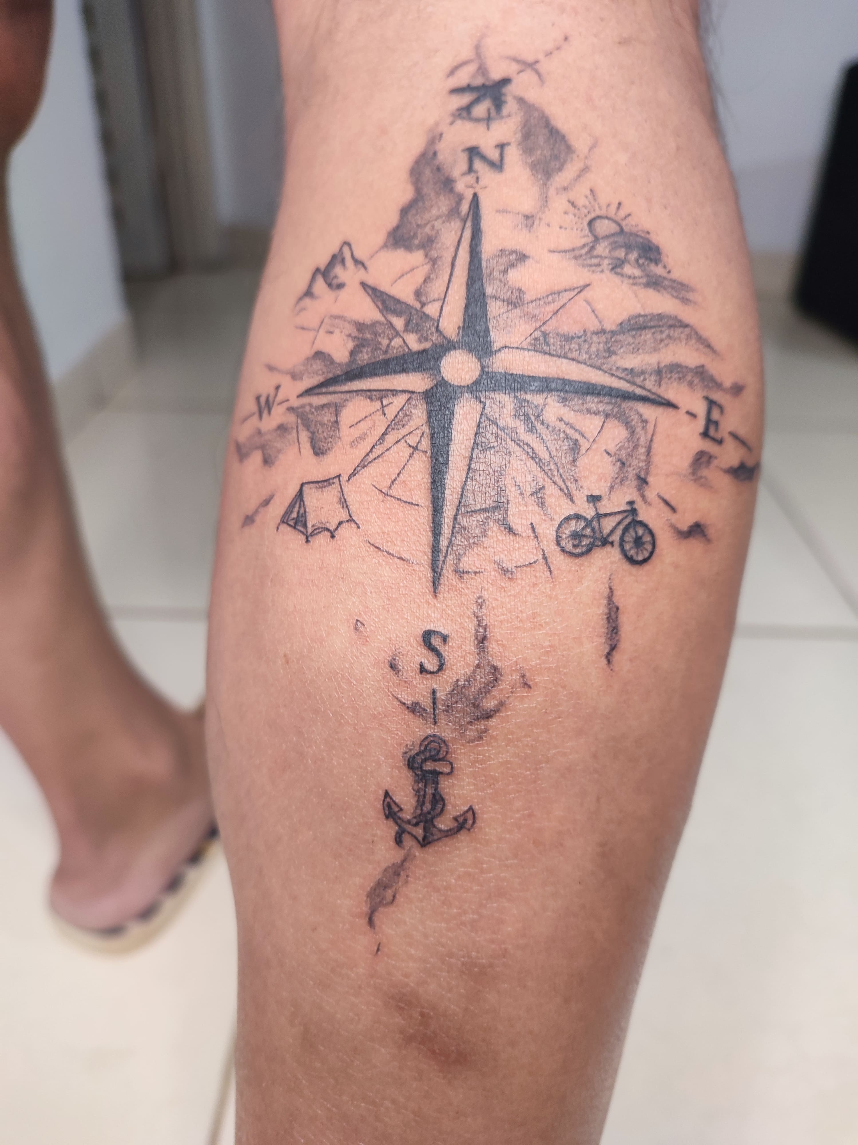 Tatuagem traço fino de uma Bússola com suas pontas voltadas para viagens, de cada lado 