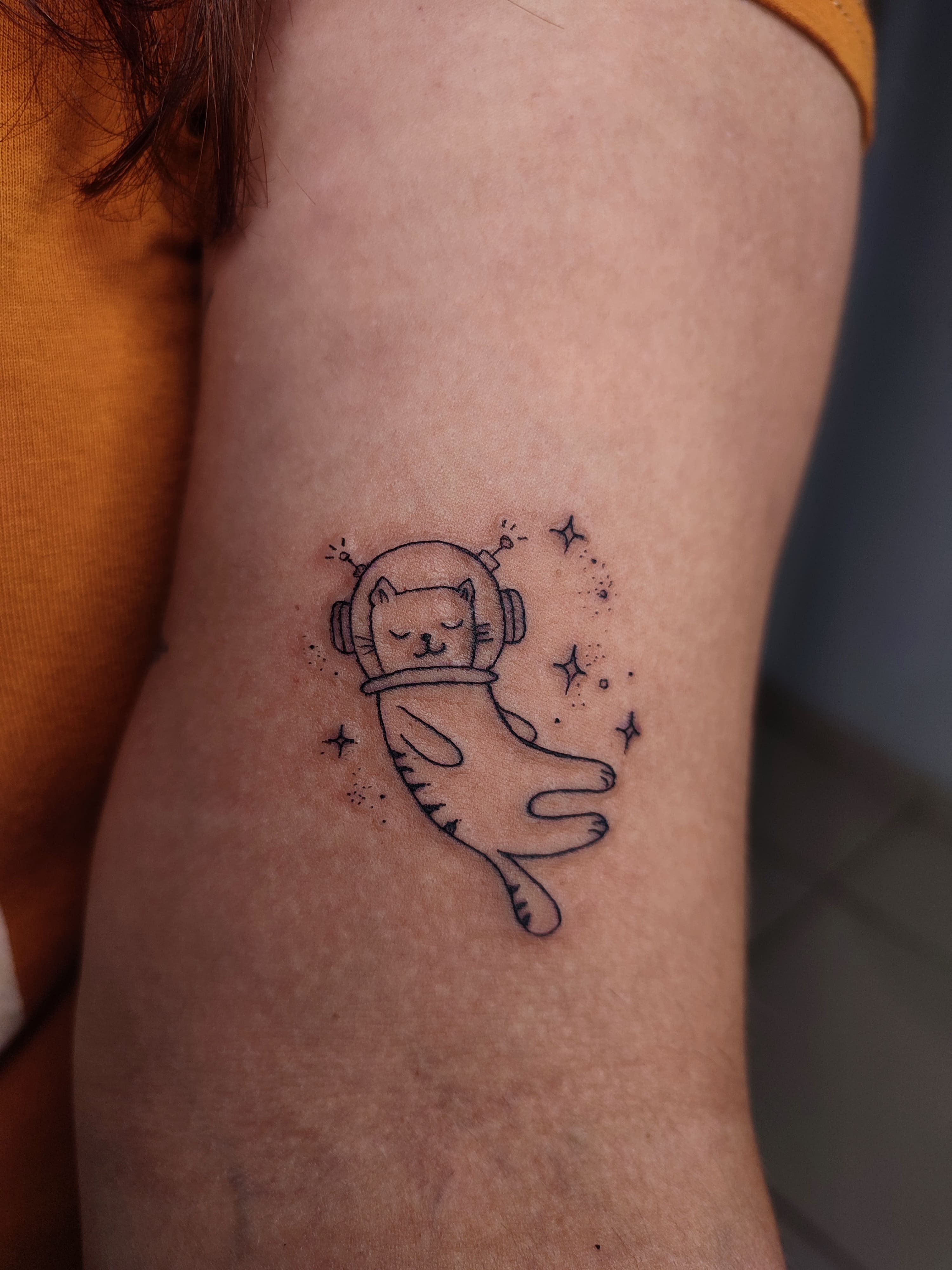 Tatuagem de um gato astronalta no espaço ouvindo musica