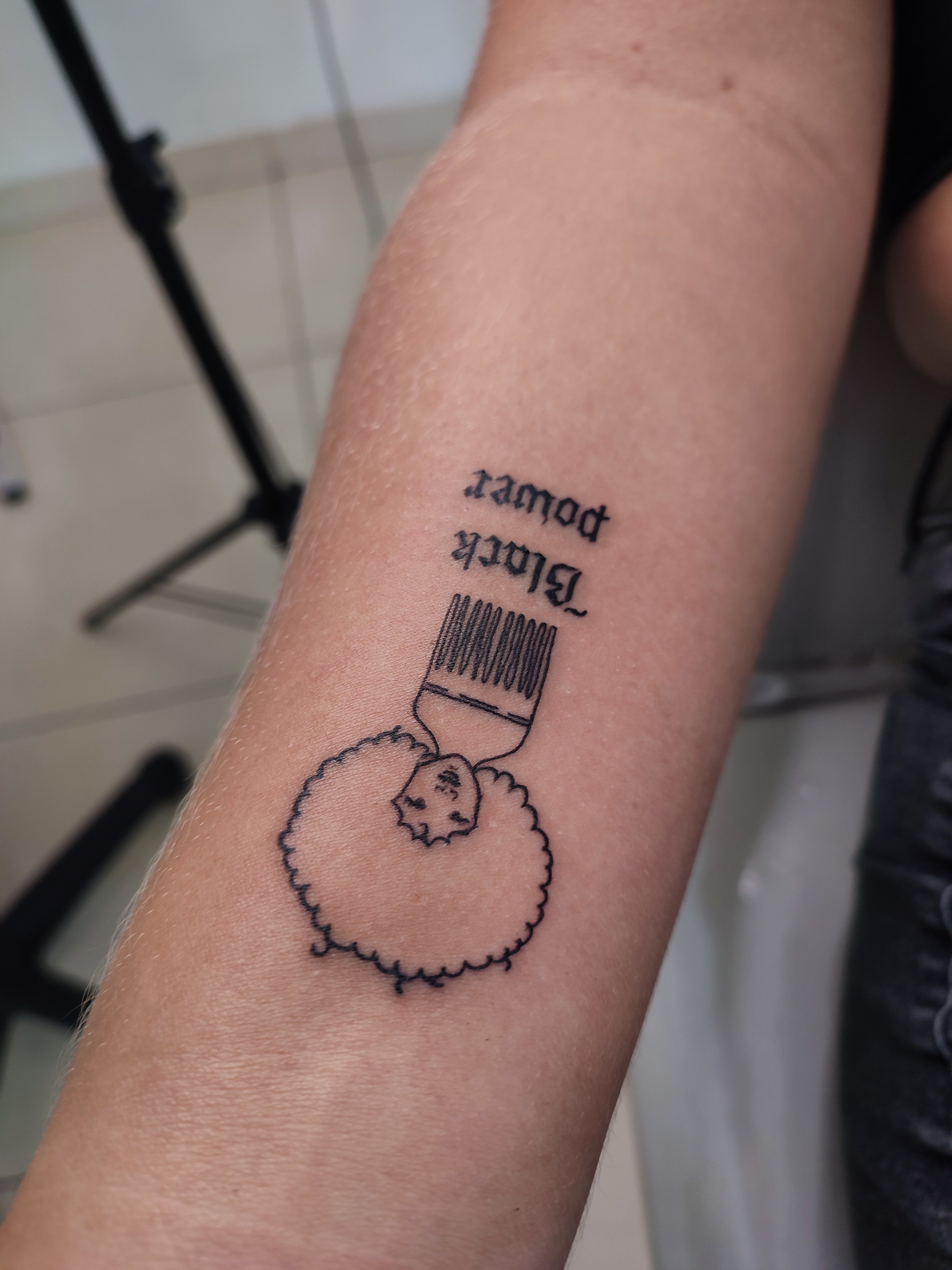 Tatuagem minimalista de um pente com a base dele com black power