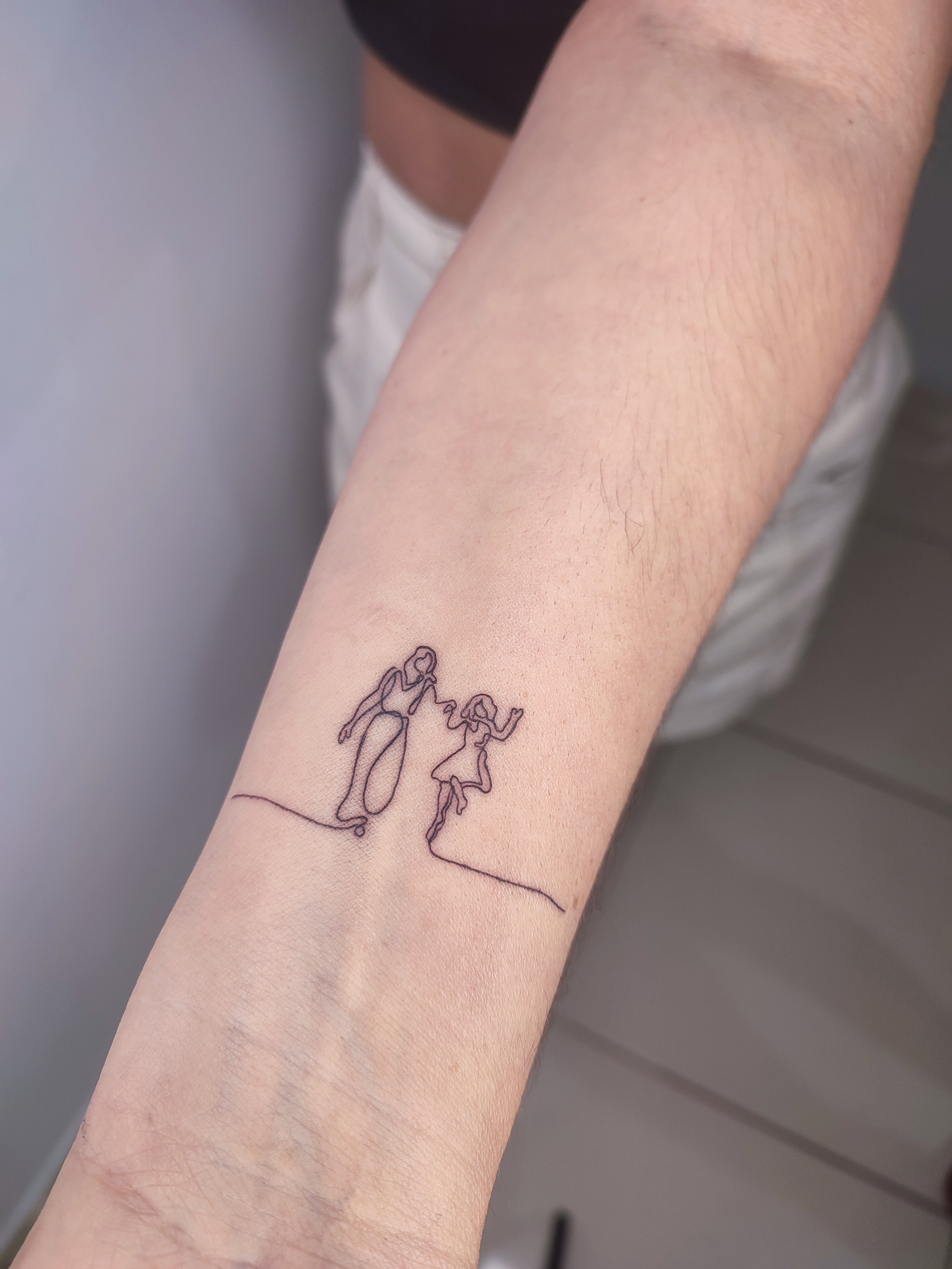 Tatuagem minimalista de duas linhas se encontrando e formando uma imagem de duas mulheres, que é a mae e sua filha