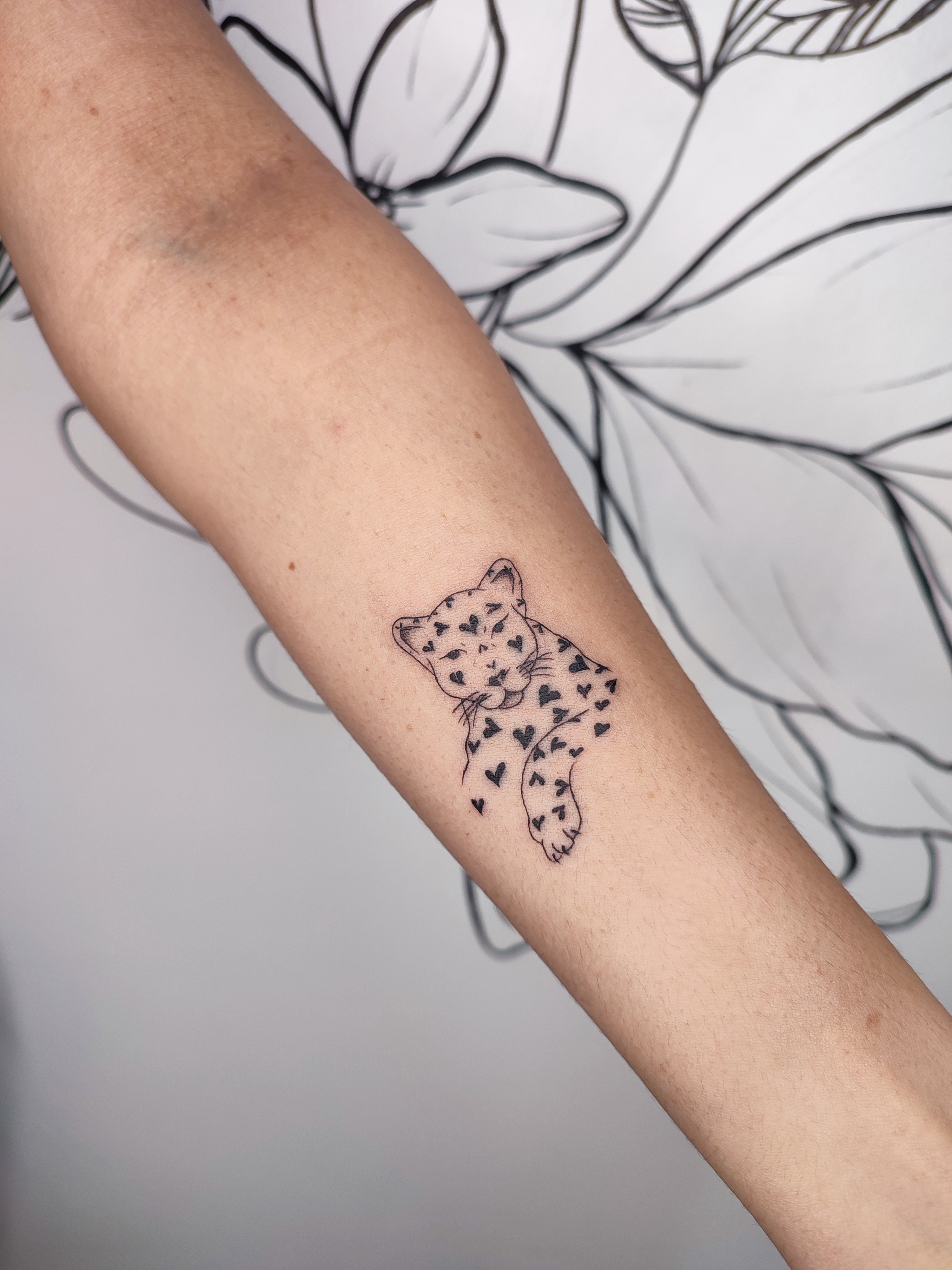 Tatuagem minimalista de uma onça pintada, mas as pintas sao coraçoês