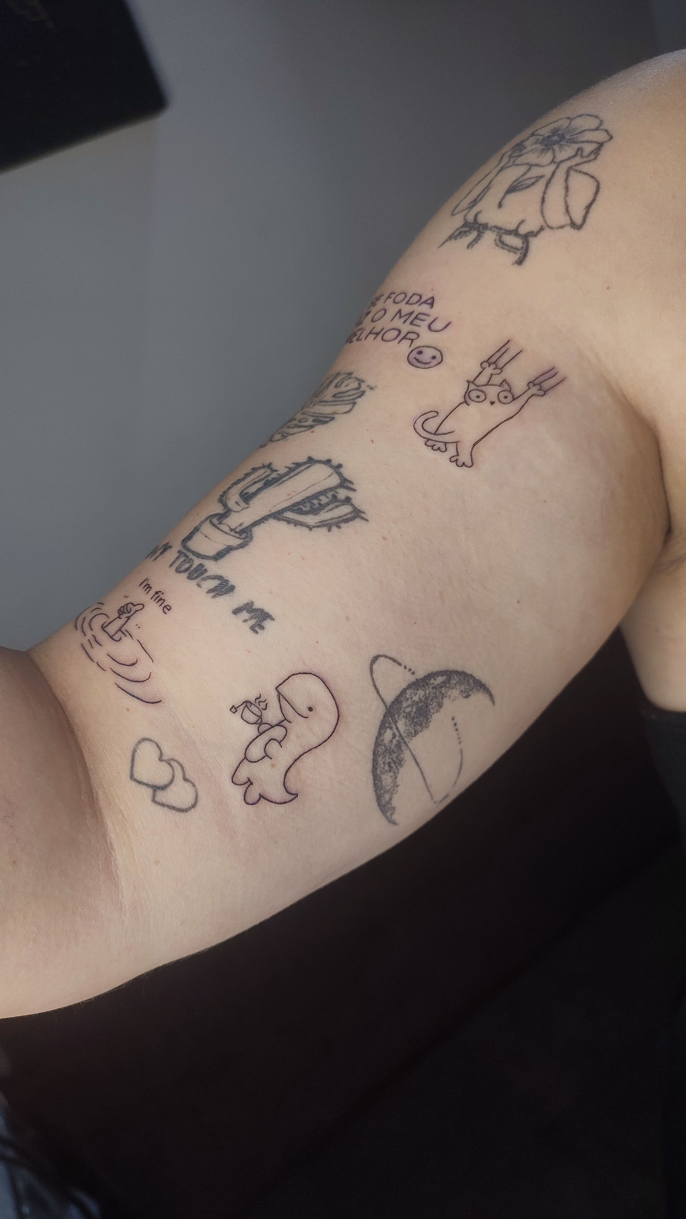 Tatuagem minimalista de um gato, um dinossauro e um cacto