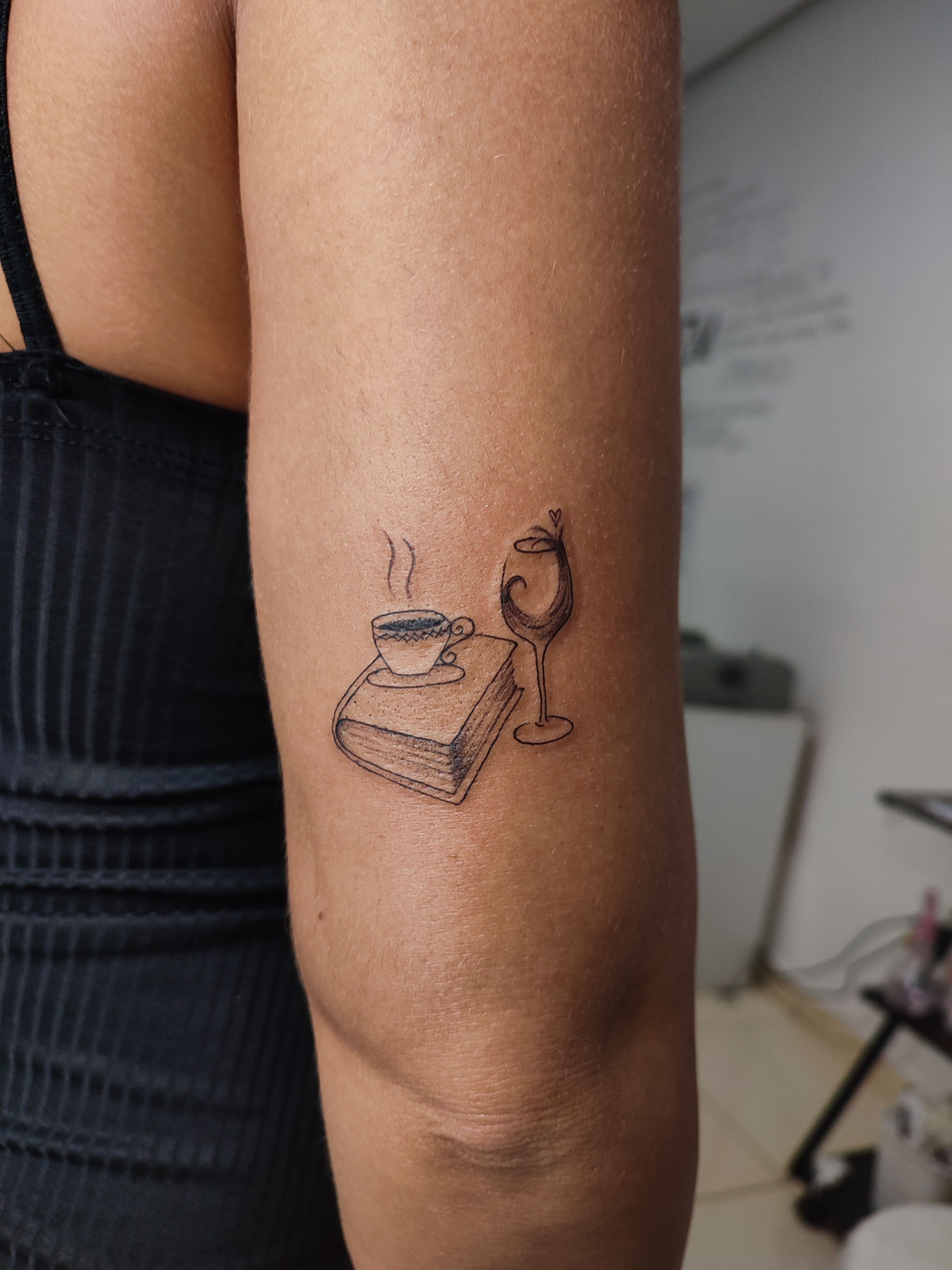 Tatuagem minimalista de um cafe e o livro