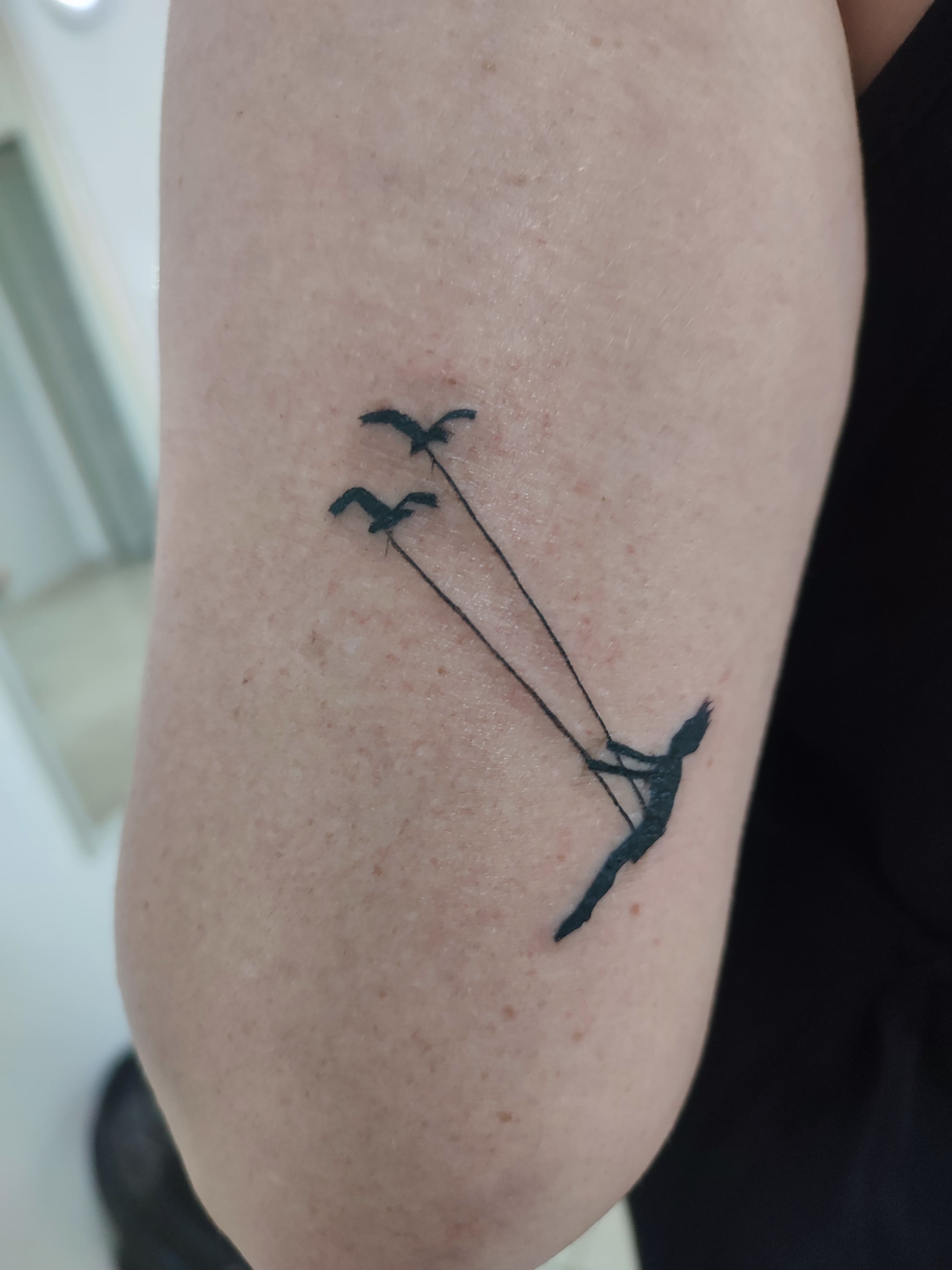 Tatuagem minimalista de um balanço com o apoio das cordas sendo dois passárinhos